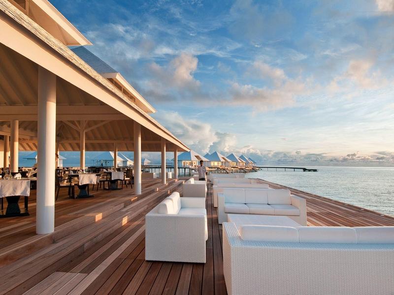 Offener Terrassenbereich mit weißen Sitzmöbeln und Meerblick bei Sonnenuntergang