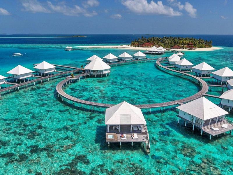 Luxuriöse Überwasserbungalows auf türkisfarbenem Wasser mit klarem Himmel und Insel im Hintergrund