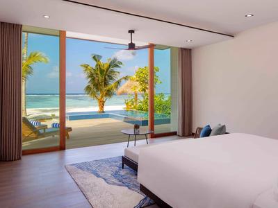 Helles Schlafzimmer mit offenem Panoramafenster, Blick auf Pool, Palmen und türkisfarbenes Meer.