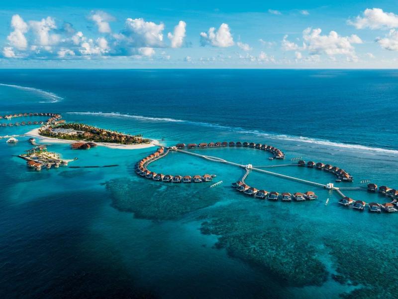 Luxuriöse Überwasserbungalows erstrecken sich über türkisfarbenes Meer unter blauem Himmel.