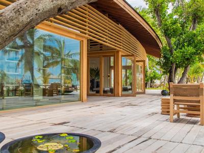 Moderní hotelová terasa s dřevěnou podlahou, jezírky a stinným stromem.