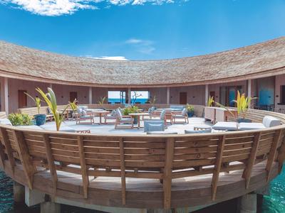 Nadvodní bungalov s terasou a posezením nad čistou vodou pod modrou oblohou.