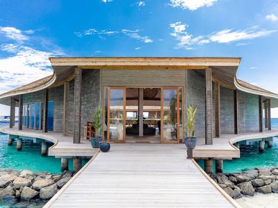 Luxusní vila nad vodou s dřevěným molem a tyrkysovým mořem pod modrou oblohou.