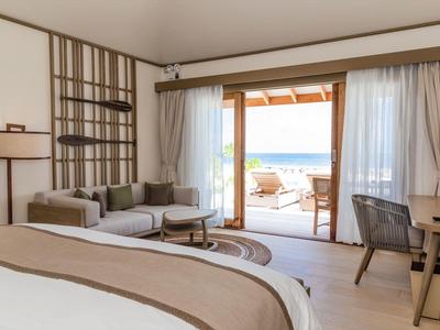 Světelný hotelový pokoj s postelí, pohovkou a výhledem na terasu u moře.