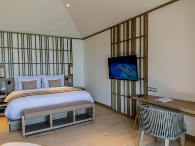 Bright hotel room with large bed, wall-mounted TV, and desk with chair.