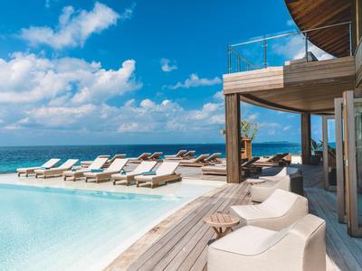 Luxurious resort with pool, lounge chairs, and sea view under a sunny sky.