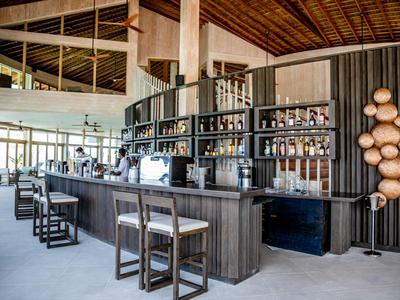 Moderní hotelový bar s dřevěným pultem, barovými židlemi a policemi s lihovinami.