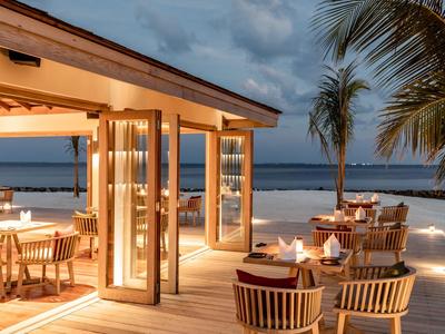 Příjemná restaurace s výhledem na moře, dřevěnou terasou a tropickými rostlinami za soumraku.