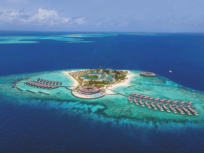 Letecký pohled na tropický ostrov s resortem a bungalovy nad vodou v průzračném tyrkysovém moři.