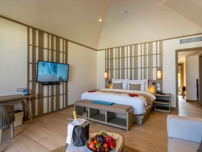 Moderní hotelový pokoj s velkou postelí, televizí, psacím stolem a posezením.