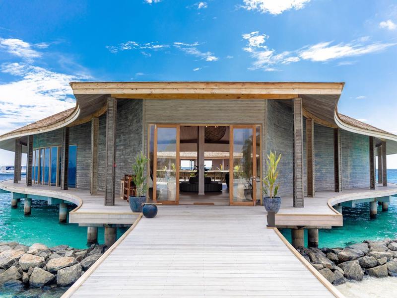 Luxusní vila nad vodou s dřevěným molem a tyrkysovým mořem pod modrou oblohou.