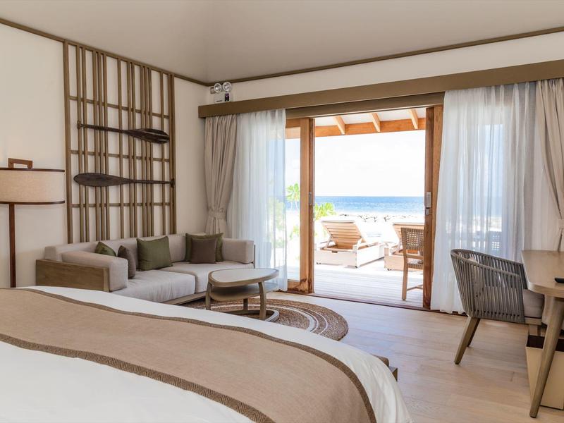 Světelný hotelový pokoj s postelí, pohovkou a výhledem na terasu u moře.