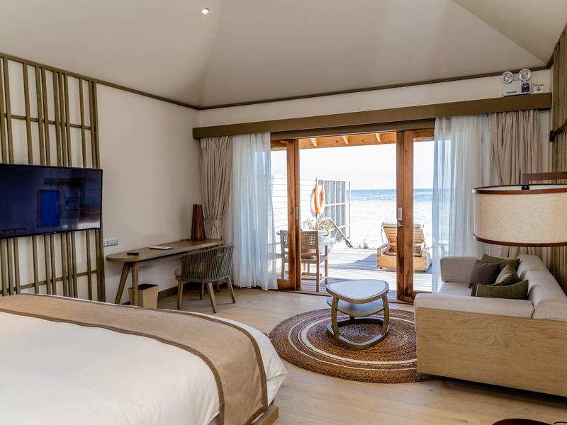 Světle zařízený hotelový pokoj s výhledem na moře a balkonem s posezením.