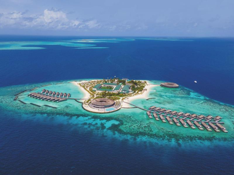 Letecký pohled na tropický ostrov s resortem a bungalovy nad vodou v průzračném tyrkysovém moři.