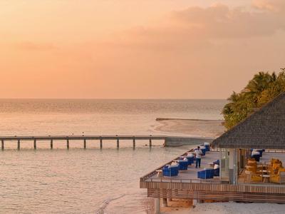 Atardecer sobre vista al mar con muelle, casa de playa y zona de asientos.