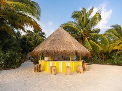 Choza de bar de playa amarilla con techo de paja rodeada de palmeras en playa de arena blanca.
