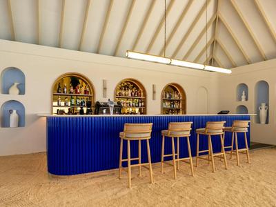 Área de bar moderna con mostrador azul y taburetes de madera en habitación luminosa con suelo arenoso