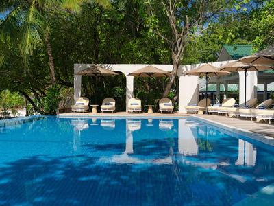 Área de piscina moderna con tumbonas y grandes pérgolas en un jardín tropical de hotel