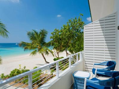 Balcón con asientos con vista a una playa tropical con palmeras y cielo azul claro.