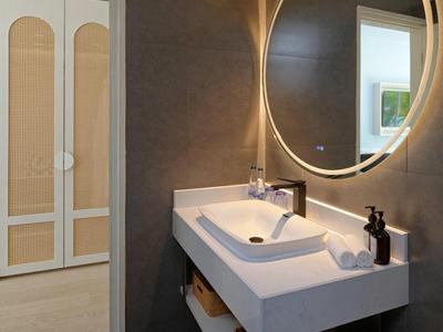 Baño moderno con espejo redondo iluminado y lavabo doble blanco.