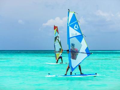 Dos personas practican windsurf en el mar turquesa bajo un cielo azul.