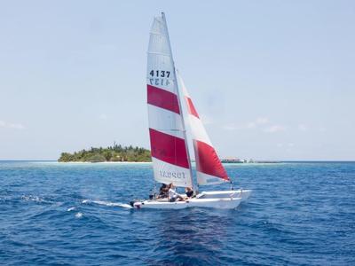 Velero con velas rojas y blancas navegando en mar abierto cerca de una pequeña isla.