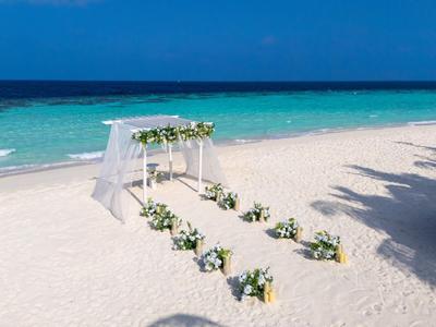 Ceremonia de boda en la playa con un arco blanco y decoraciones florales junto al mar