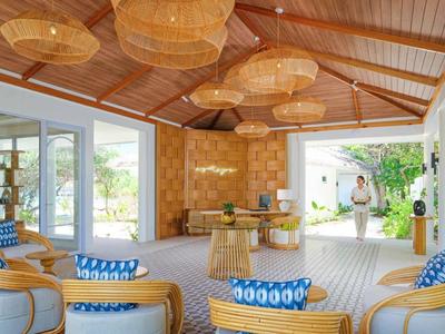 Bright hotel lobby with wooden ceiling, woven lamps, and pastel-toned seating areas.