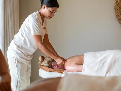 Masseuse massages relaxed guest in calm spa setting.