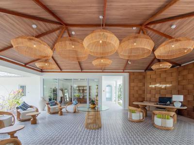 Bright hotel lounge with wooden ceiling, woven lamps, and cozy seating areas.