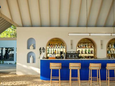 Modern hotel bar area with blue counter, wooden stools, and white rounded arches in the background.