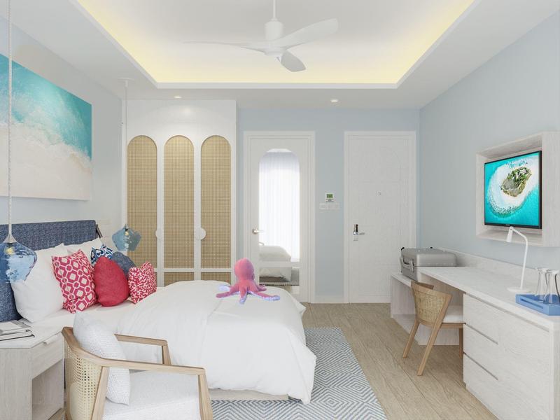 Bright hotel room with white bed, desk, chair, ceiling fan, and island artwork.