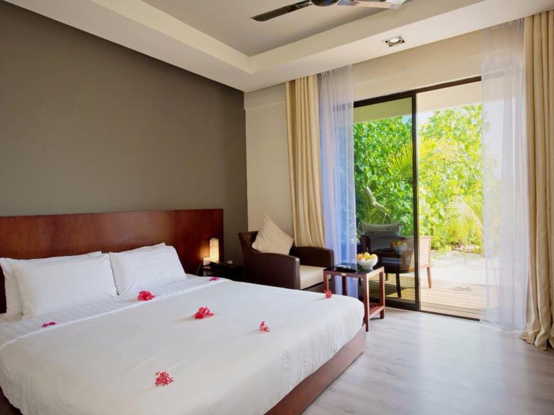 Modern hotel room with double bed and balcony door to green garden.