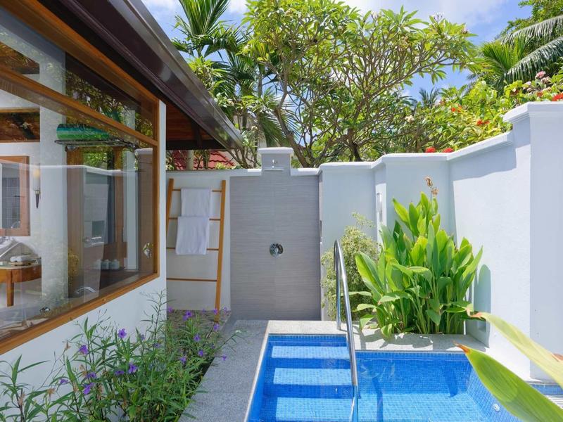 Small pool with stairs next to outdoor area of a house with garden plants.