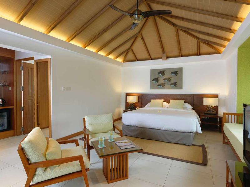 Cozy hotel room with large bed, seating area, ceiling fan, and warm lighting.