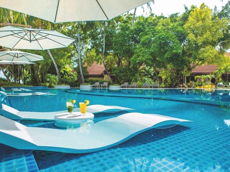 Swimming pool with built-in loungers and umbrellas in tropical hotel garden.