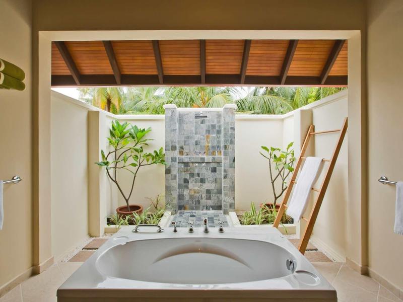 Freestanding bathtub with faucets in front of mosaic stone wall in open bathroom with plants.