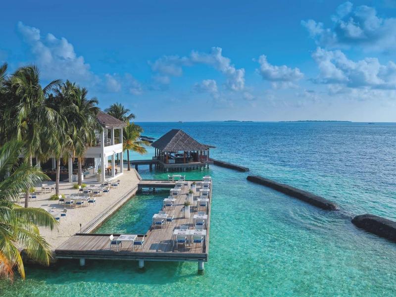 Resort with overwater bungalows, palm trees, and clear tropical sea.