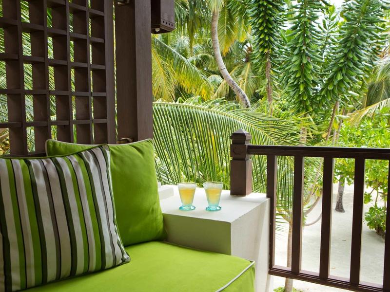 Green bench with striped cushion on a porch overlooking tropical plants
