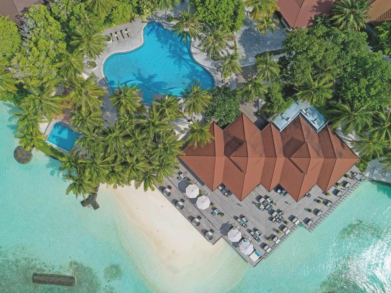 Aerial view of hotel resort with tropical pool, sandy beach, and turquoise sea.