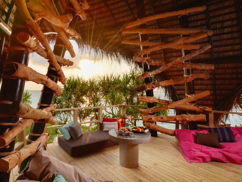 Coin lounge confortable avec sol en bois, canapés et décoration tropicale sous un toit en bois.