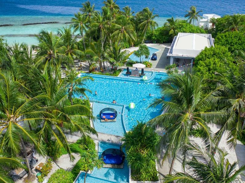 Zone de piscine luxueuse dans une station balnéaire tropicale avec des palmiers et vue sur l'océan.