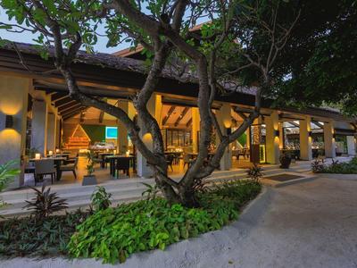 Espace restaurant ouvert avec tables et chaises entouré d'arbres et de plantes dans un hôtel.