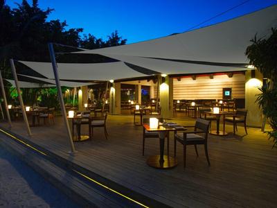 Salon extérieur confortable avec tables, chaises et toiles d'ombrage dans une ambiance calme du soir.