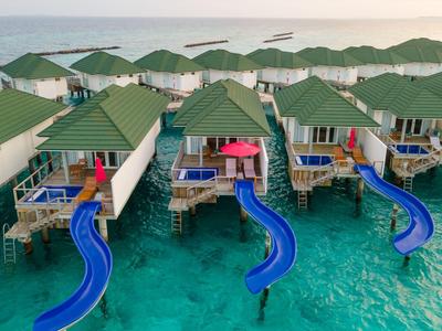 Reihen von Wasserbungalows mit grünen Dächern und blauen Wasserrutschen über türkisfarbenem Meer.