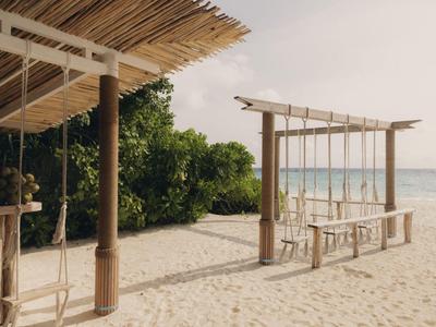 Ein entspannter Strand mit einem schattigen Holzpavillon und einer Schaukel mit Meerblick.