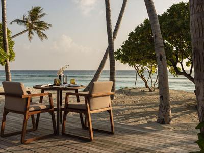 Tisch mit Stühlen am Strand unter Palmen mit Blick auf das Meer bei Sonnenuntergang.