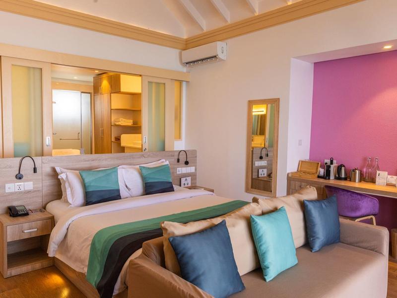 Modern eingerichtetes Hotelzimmer mit Doppelbett, Sofa und Schreibtisch mit Kaffeemaschine.