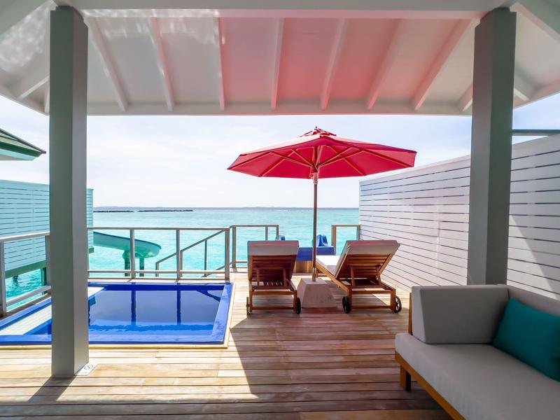 Terrasse mit Pool, Liegestühlen und rotem Sonnenschirm mit Meerblick.