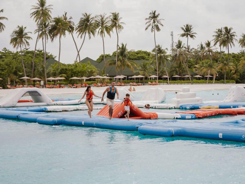 Menschen genießen Wasserspielplatz mit Palmenstrand im Hintergrund.